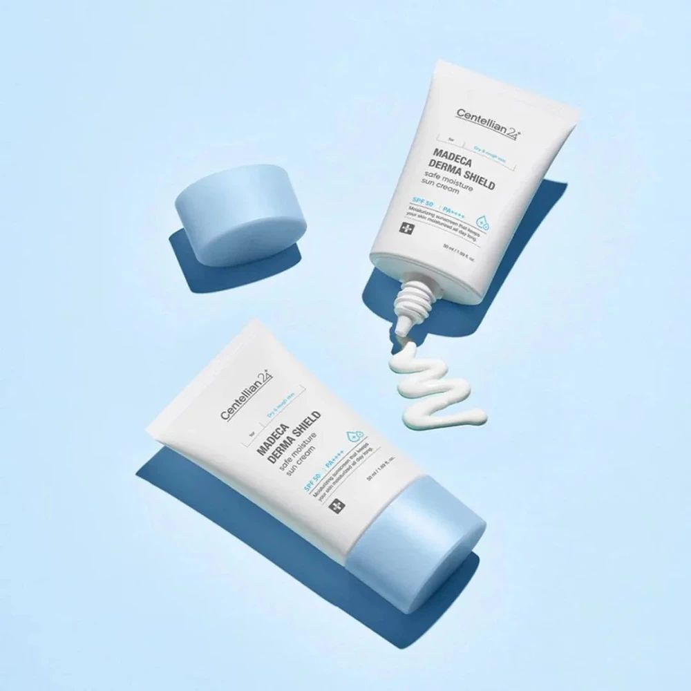 Drei Tuben Sonnencreme auf blauem Hintergrund. Eine mit geöffnetem Deckel, eine mit Creme, die herausquillt. Aufschrift: MADECA DERMA SHIELD safe moisture sun cream.