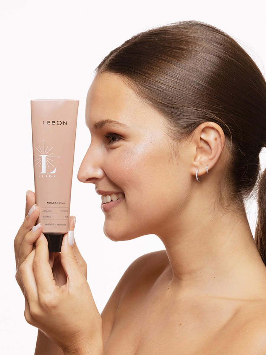Person hält eine Tube Zahnpasta. Auf der Tube steht LEBON und NOACARLINA. Die Person lächelt.