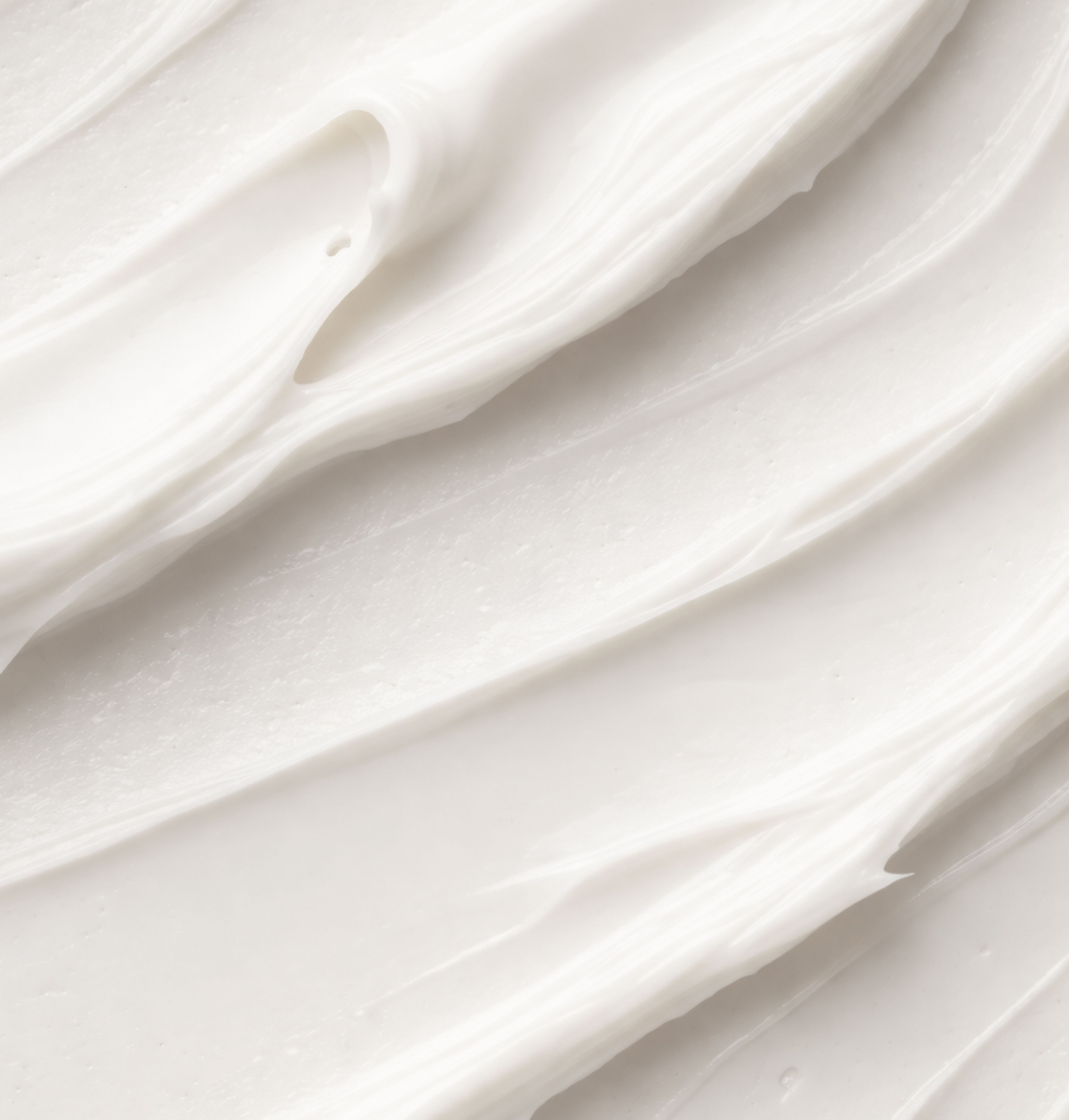 Nahaufnahme von cremiger, weißer Substanz. Textur mit wellenförmigen Strukturen.