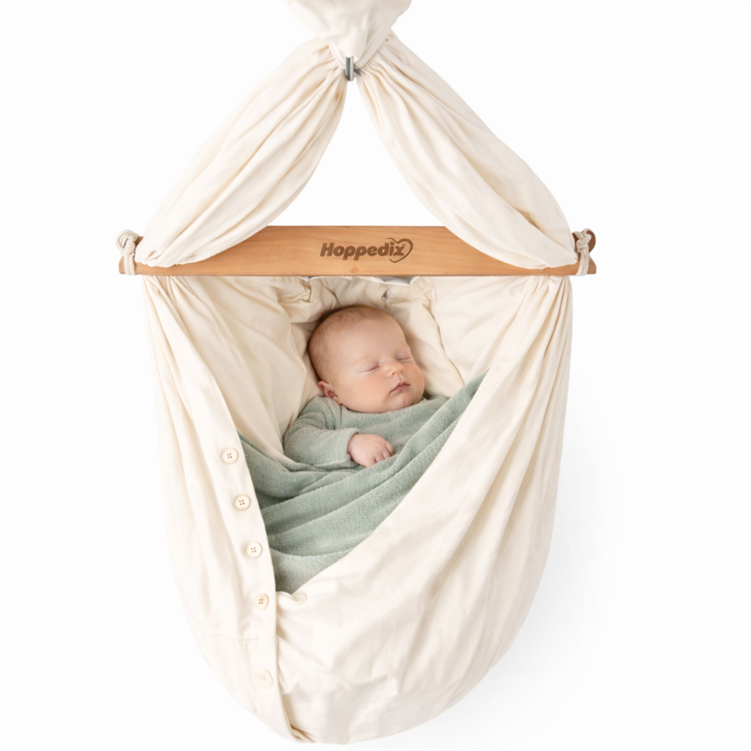 Baby in cremefarbener Federwiege mit Holzstange. Auf der Stange steht "Hoppediz". Baby liegt zugedeckt.