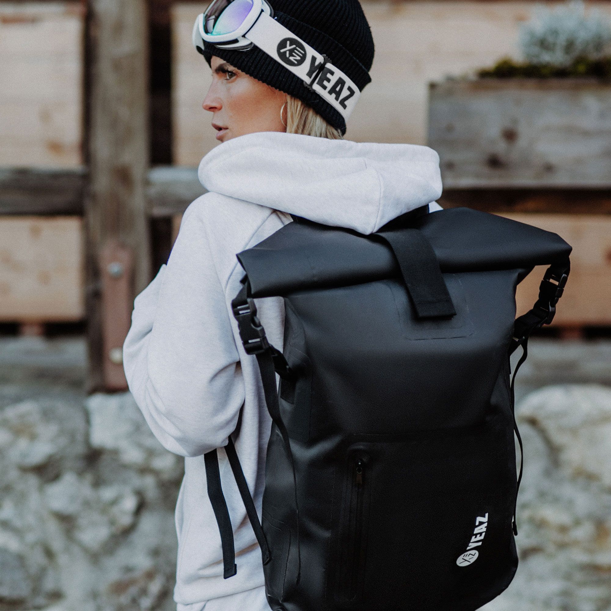 Person trägt schwarzen, wasserdichten Rucksack. Rollverschluss, weißes Logo, im Freien.