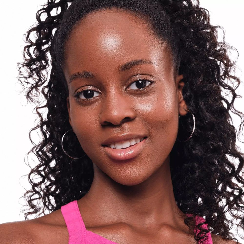 Porträt einer dunkelhäutigen Frau mit lockigem Haar. Sie trägt ein pinkfarbenes Top und Ohrringe. Sie lächelt.