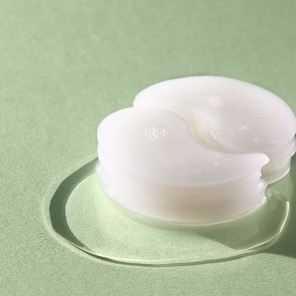 Stapel von weißen Augen-Pads auf einer Flüssigkeitsoberfläche. Grüner Hintergrund.