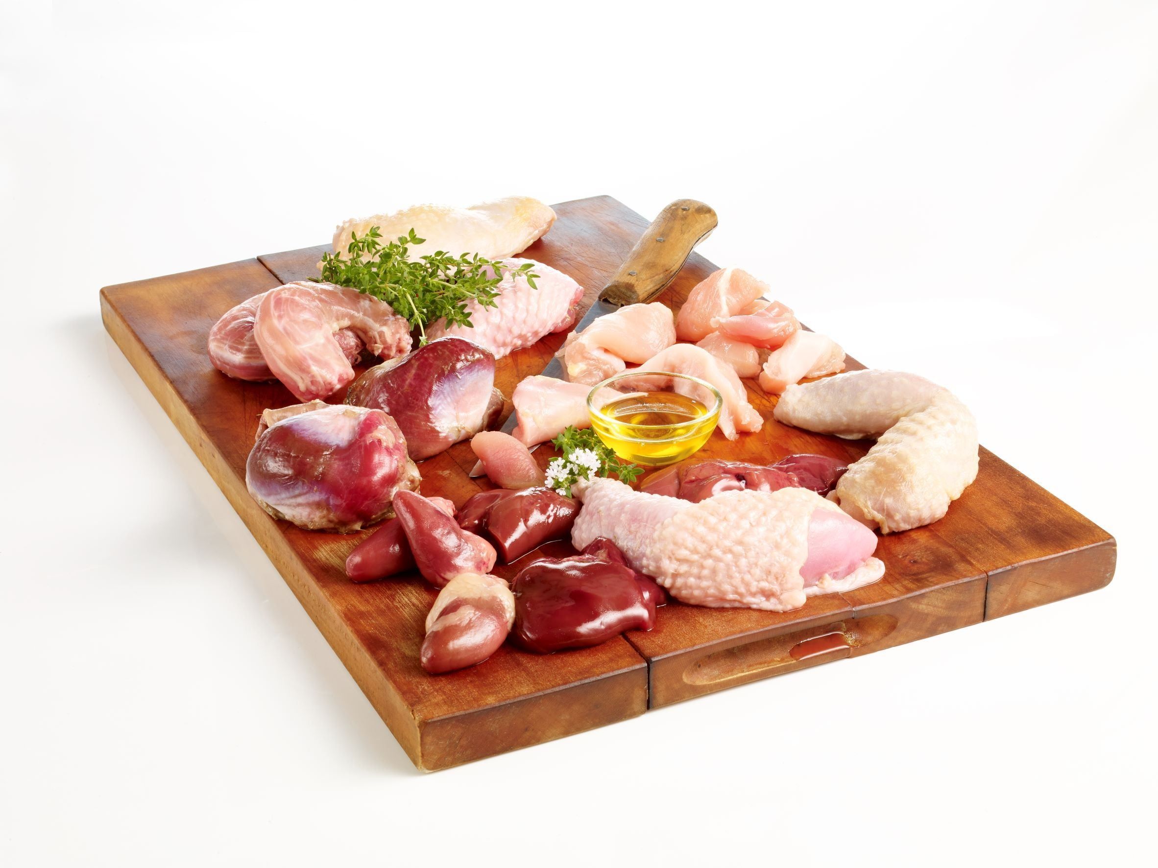 Holzbrett mit verschiedenen rohen Fleischstücken, darunter Hühnchen, Innereien und Öl. Auf dem Brett liegt auch Grünzeug.