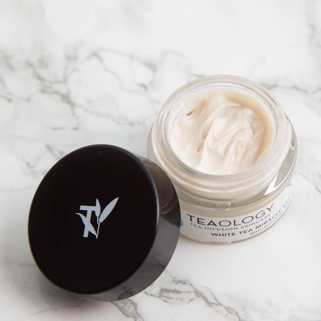 Creme in einem Glasbehälter mit offenem Deckel. Auf dem Etikett steht "Teaology" und "White Tea Miracle Anti-Age Cream".