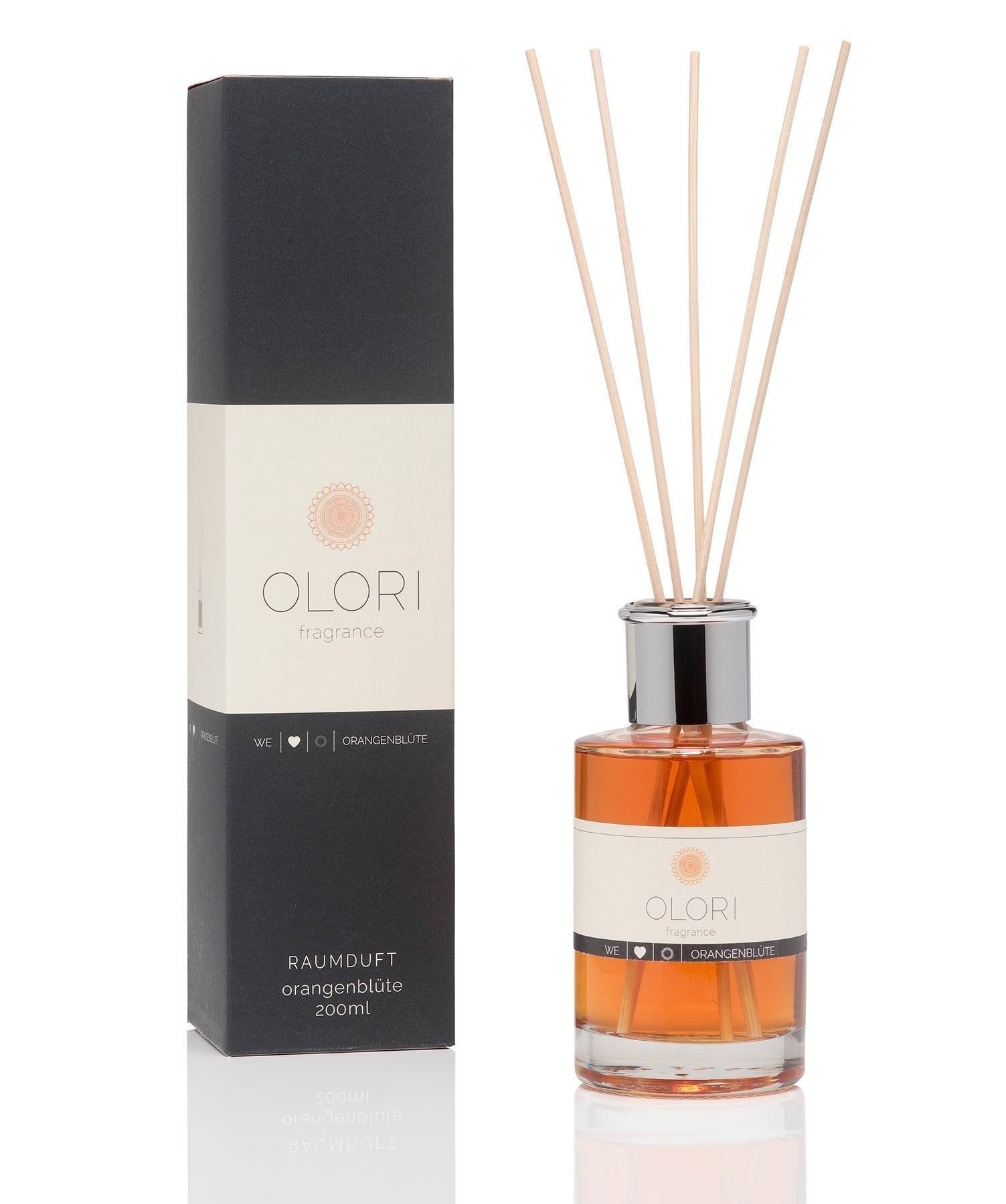 Raumduft-Diffusor mit Holzstäbchen. Flakon mit orangefarbener Flüssigkeit. Schwarze und cremefarbene Verpackung mit Logo und Produktbezeichnung.