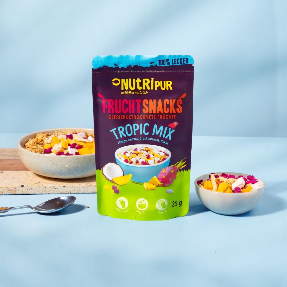 Beutel mit gefriergetrockneten Früchten. Aufschrift: NutriPur, Tropic Mix. Daneben Schale mit Müsli und Früchten.