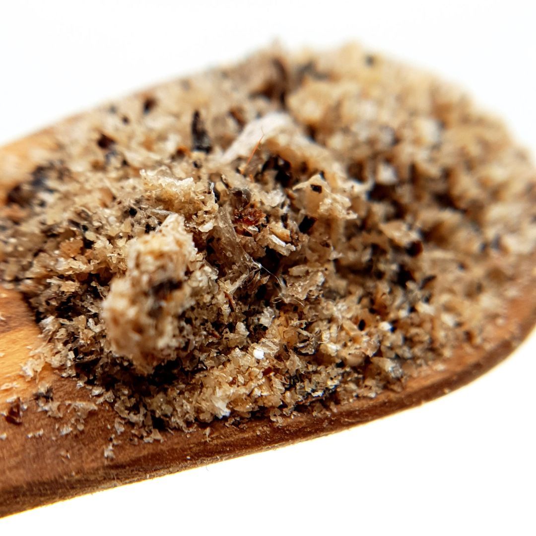 Holzlöffel mit QCHEFS Zahnputzflocken. Die Flocken sind körnig und von hell- bis dunkelbrauner Farbe.