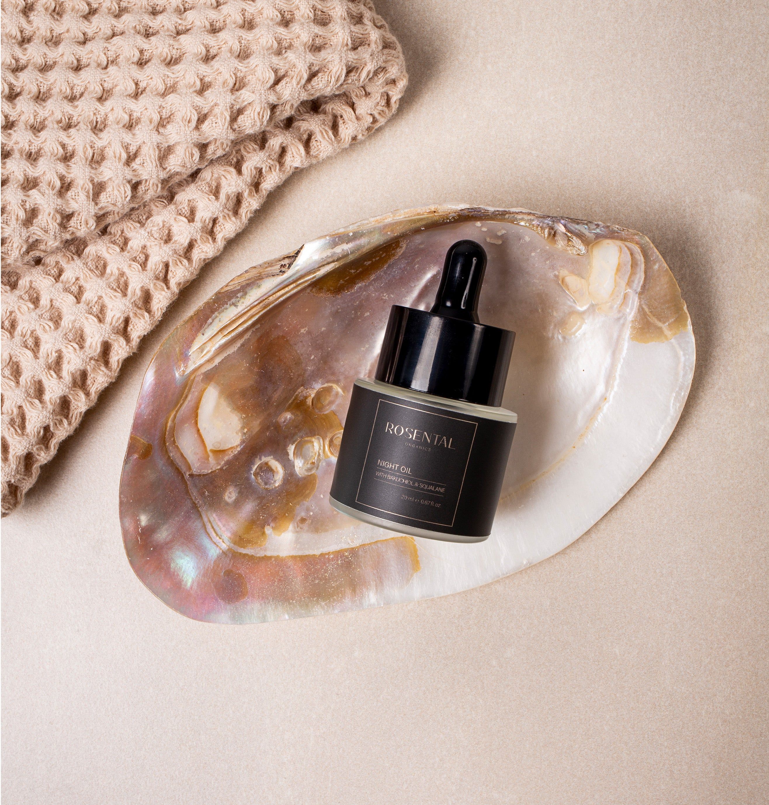 Fläschchen mit schwarzem Deckel und Pipette in einer Muschelschale. Aufschrift: Rosental Organics. Neben einem Handtuch.
