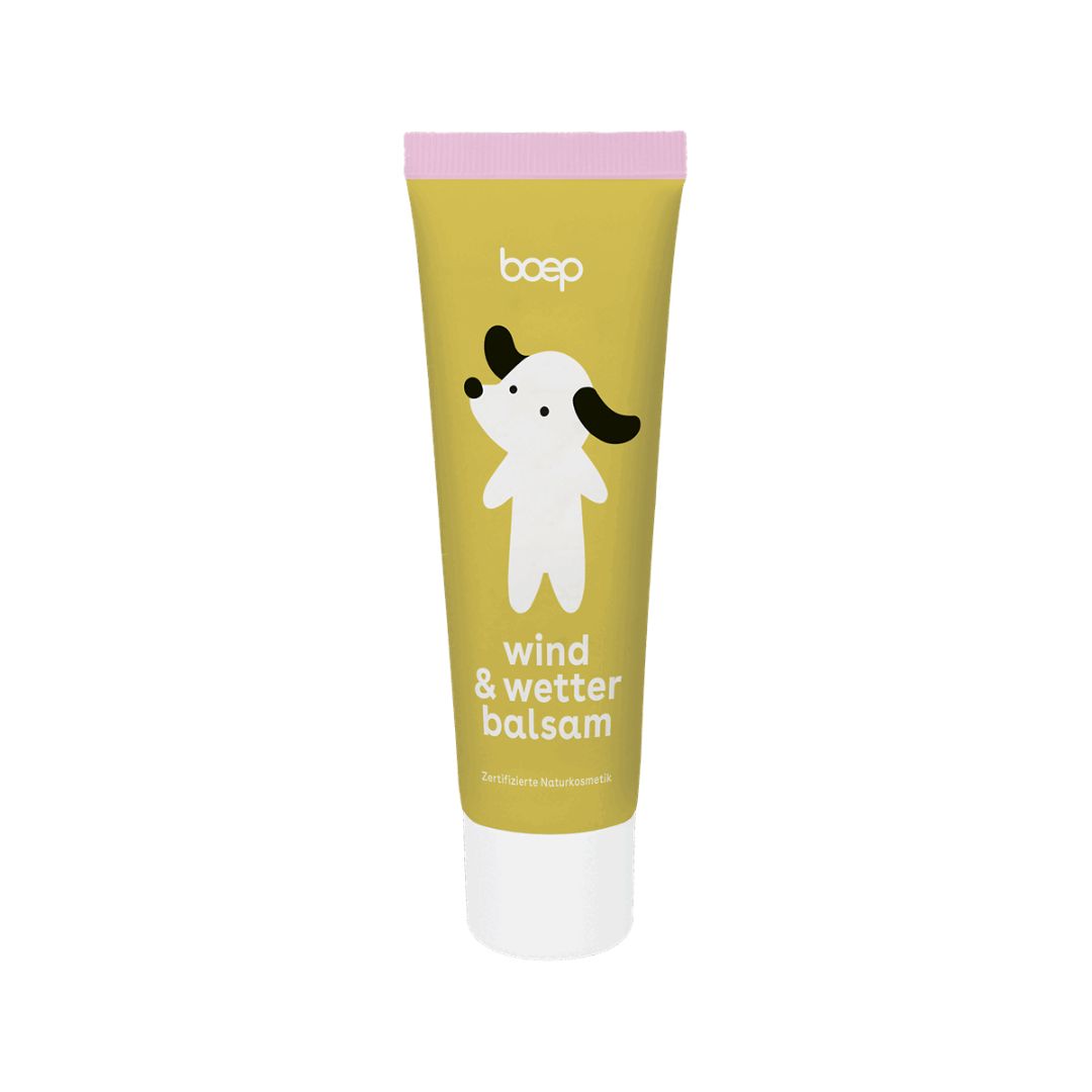 Gelbe Tube mit Hund-Illustration. Text: "wind & wetter balsam". Rosa Deckel. Weißer Boden. Zertifizierte Naturkosmetik.