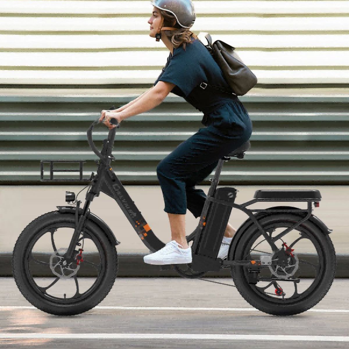 Person fährt auf einem schwarzen Elektrofahrrad. Trägt Helm und Rucksack. Hintergrund: Gebäude mit horizontalen Streifen.