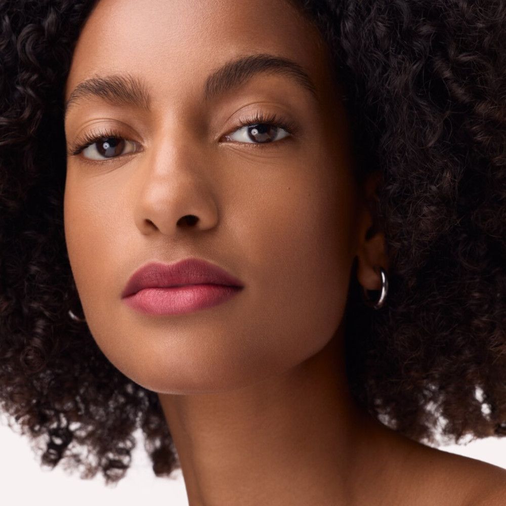 Porträt einer Frau mit rosafarbenem Lippenstift. Sie trägt silberne Creolen.