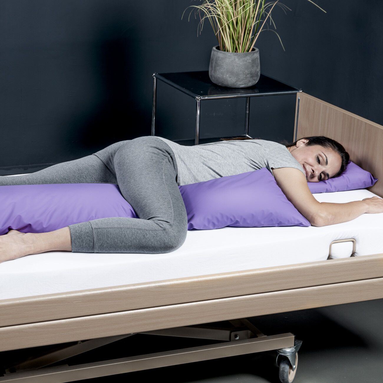 Eine Frau liegt auf einem Bett. Sie wird von zwei lila KUBIVENT PurplePos VariMed Positionierungskissen gestützt. Das Kissen ist rechteckig.