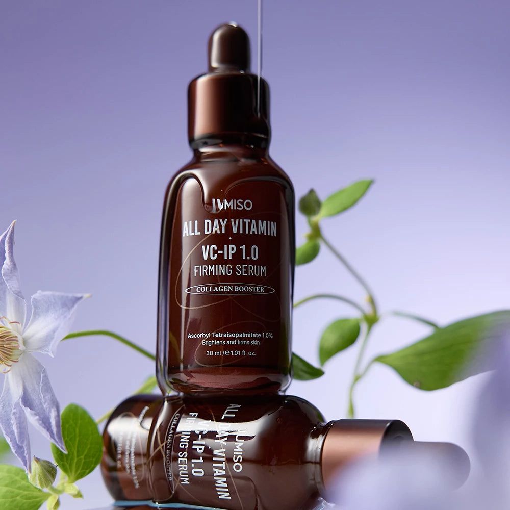 Zwei JUMISO All Day Vitamin VC-IP 1.0 Firming Serum Flaschen gestapelt mit Blumen.