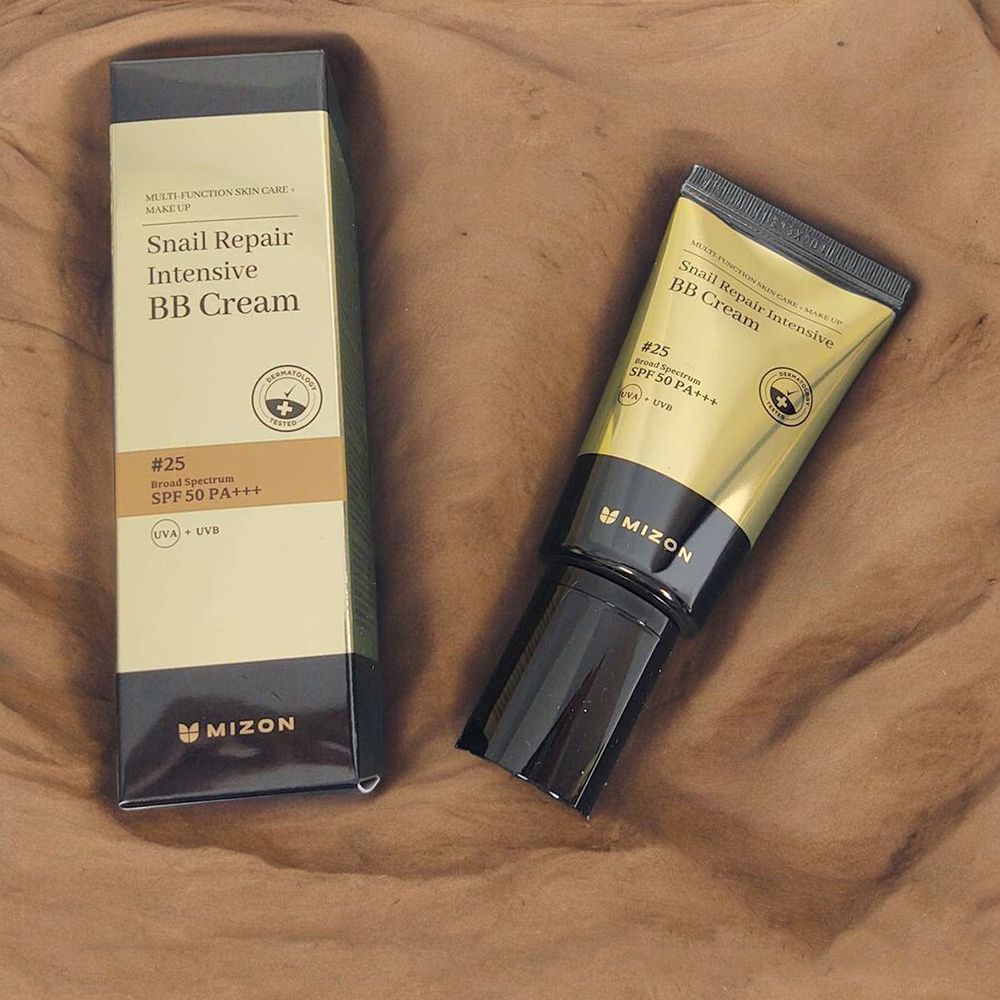 BB Cream Tube und Verpackung. Goldfarben, schwarz. Text: Snail Repair Intensive BB Cream SPF 50 PA+++, #25, MIZON. Auf braunem Untergrund.
