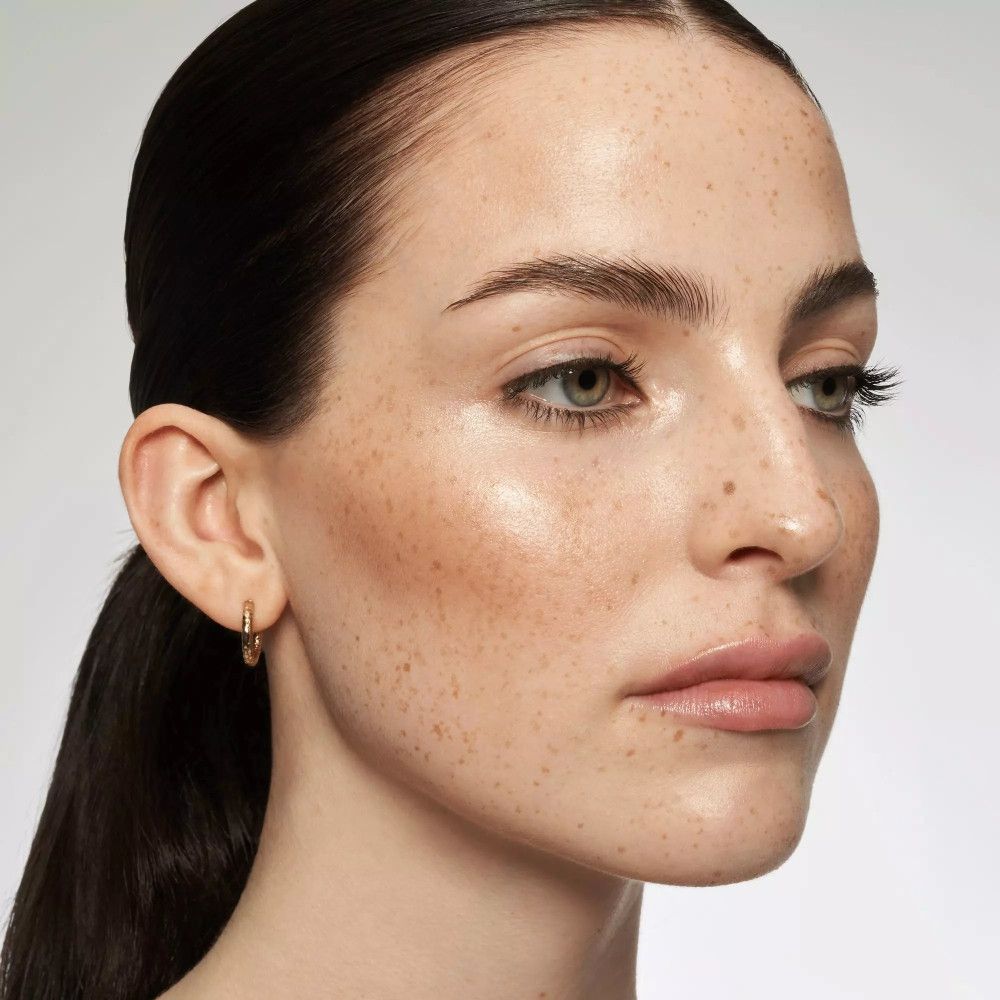 Nahaufnahme eines Gesichts mit Glanz-Tönung. Aufgetragen auf Wangen und Augenlidern. Haut mit Sommersprossen.