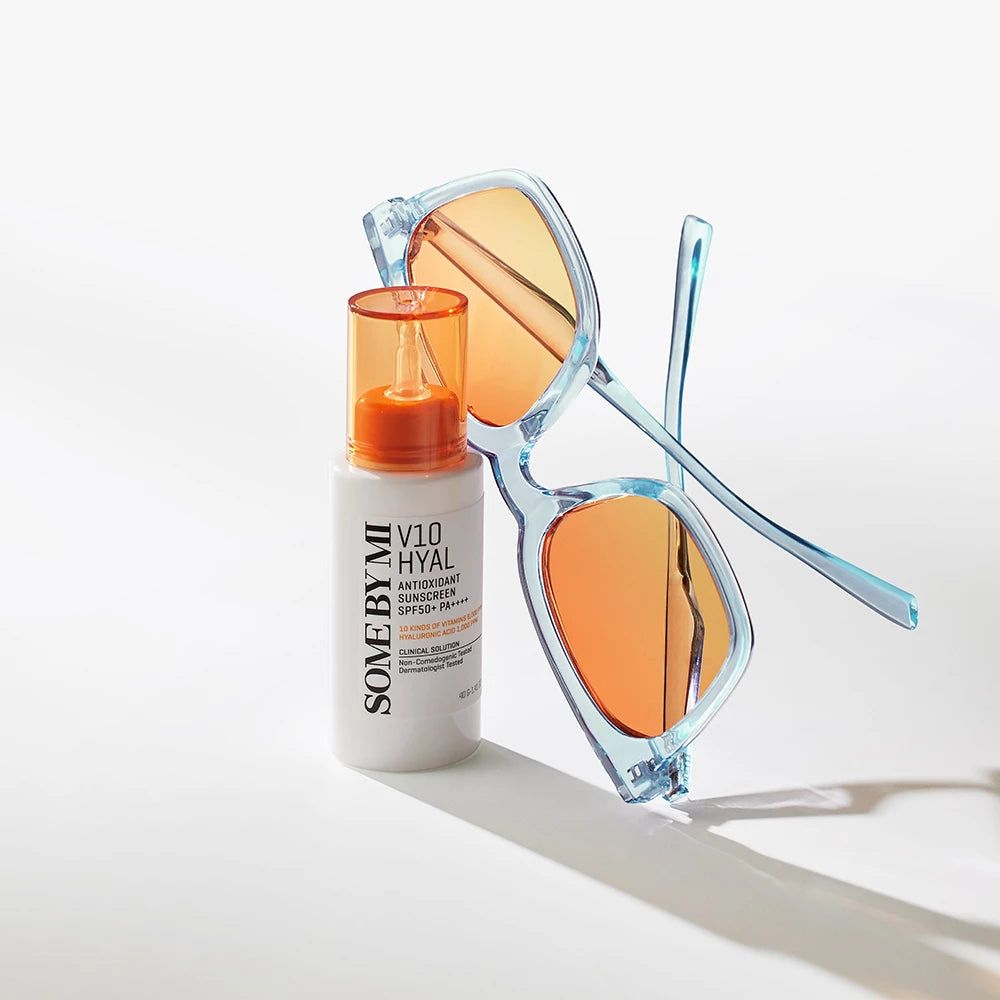 Weiße Flasche mit orangefarbenem Deckel und Sonnenbrille. Aufschrift: V10 Hyal Antioxidans Sonnenschutz SPF 50+ PA++++.