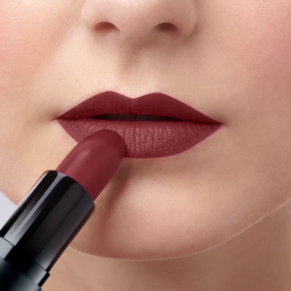 Lippenstift wird auf Lippen aufgetragen. Roter Lippenstift in schwarzer Hülse. Hautpartie mit Lippen und Lippenstift.
