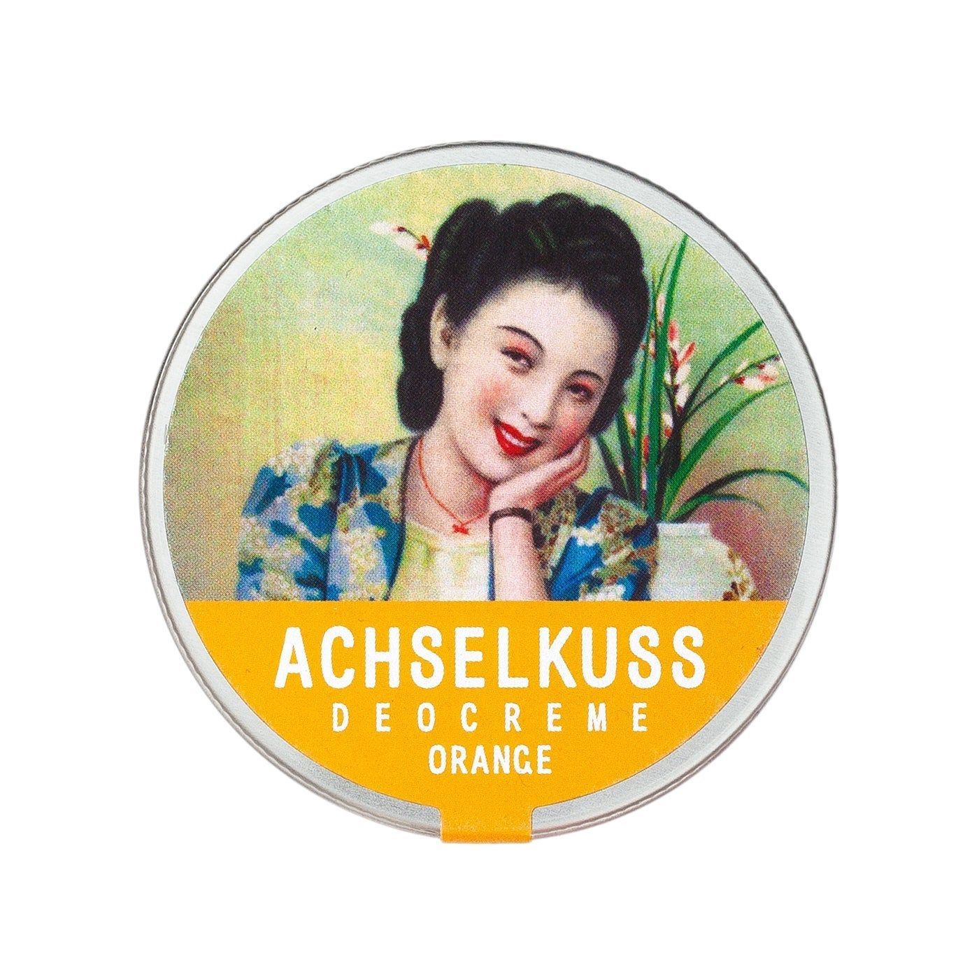 Runde Dose mit Deckel. Aufschrift: ACHSELKUSS DEOCREME ORANGE. Abbildung einer Frau mit Blumen und Topf.