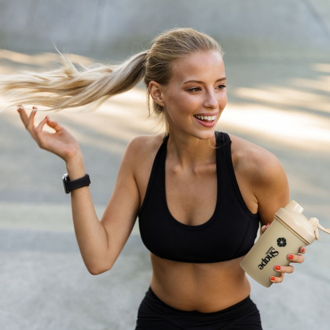 Blonde Frau mit Shake-Behälter. Der Behälter ist beige mit schwarzem Deckel. Aufschrift: Shape Republic.