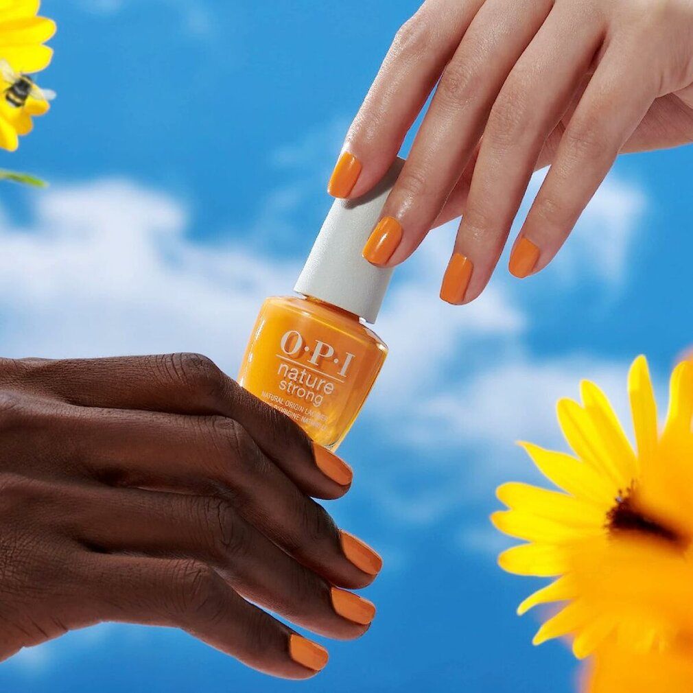 Hände mit lackierten Nägeln und Nagellackflasche. Gelb-oranger Farbton.