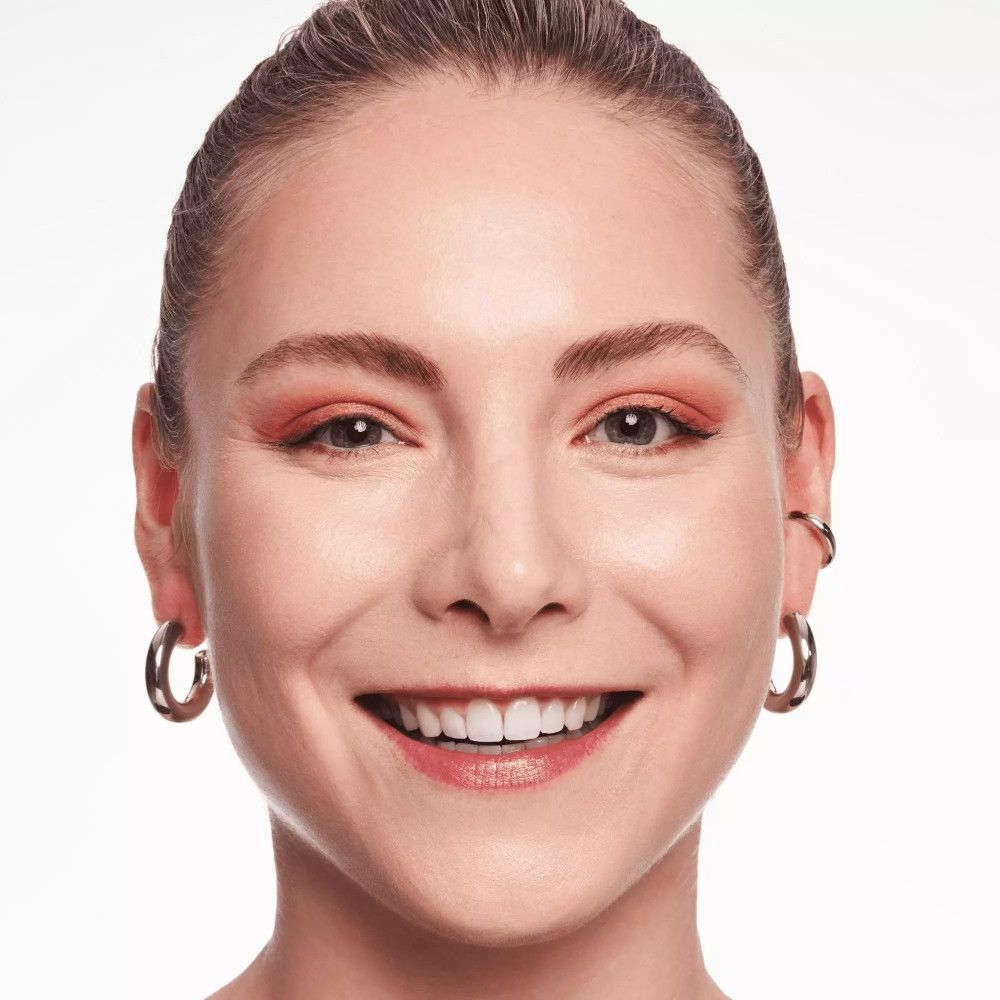 Porträt einer lächelnden Frau mit hellem Teint. Sie trägt silberne Creolen und rotes Augen-Make-up.