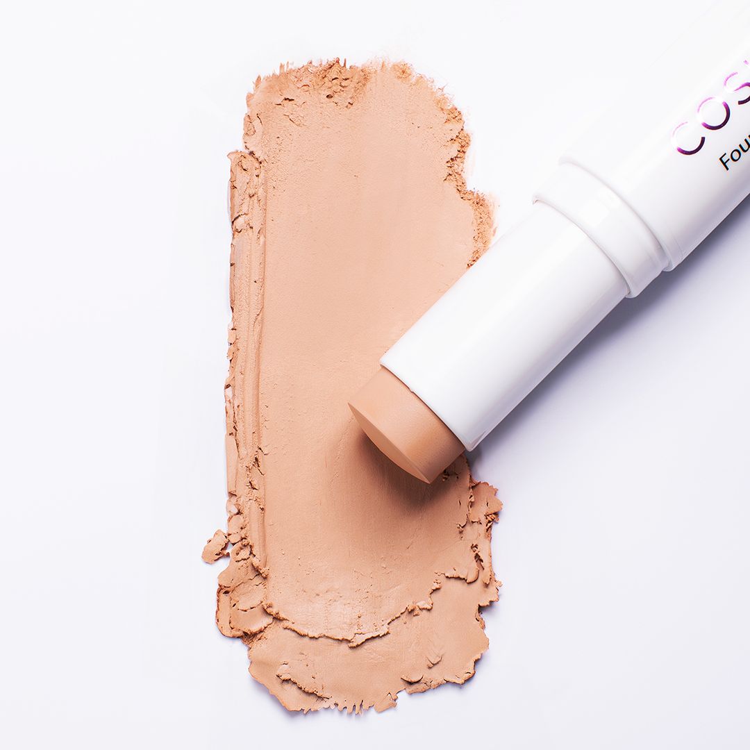 Foundation Stick liegt neben einem beigefarbenen Farbfleck. Weißer Hintergrund.