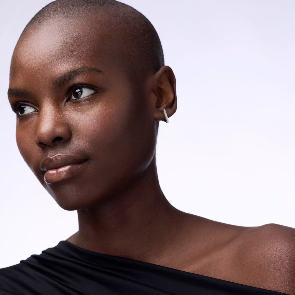 Porträt einer Frau mit dunkler Haut. Sie trägt einen schwarzen One-Shoulder-Top und Ohrringe.