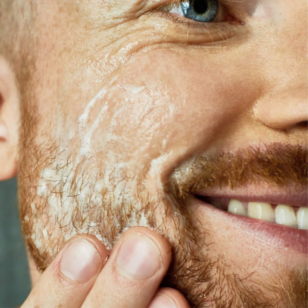 Nahaufnahme eines Mannes, der ein Peeling auf sein Gesicht aufträgt. Weißes Produkt auf der Haut.