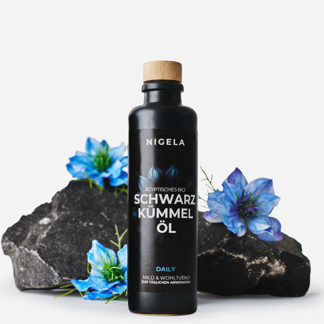 Schwarzkümmelöl-Flasche mit Holzverschluss, auf Steinen und Blüten. Aufschrift: Nigela, Ägyptisches Schwarzkümmel Öl.