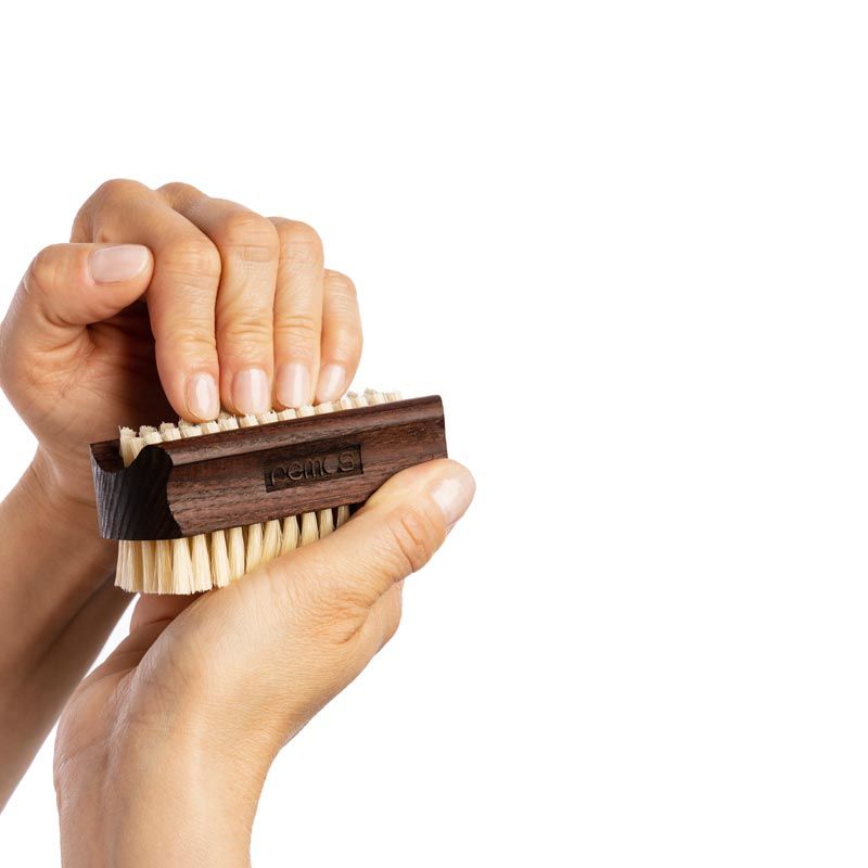 Hände benutzen eine Hand- und Nagelbürste. Borsten werden auf die Finger gedrückt. Dunkles Holz, helle Borsten.