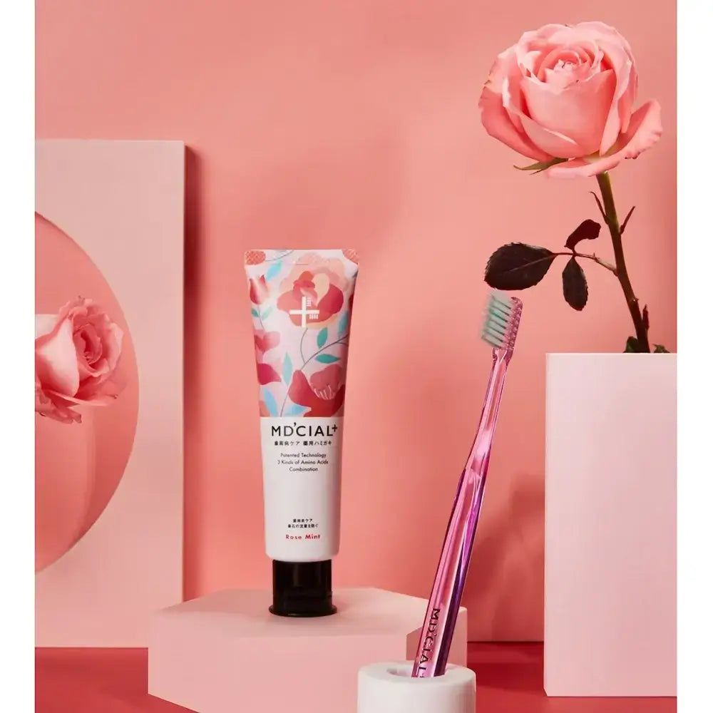 Zahnpasta-Tube, MD'CIAL+, Rose Mint, neben rosa Zahnbürste und Rose. Rosa Hintergrund.