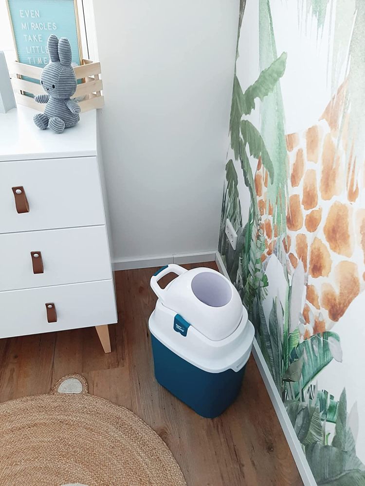 Blauer und weißer Windeleimer auf Holzboden. Neben Kommode und Wand mit Dschungel-Tapete.