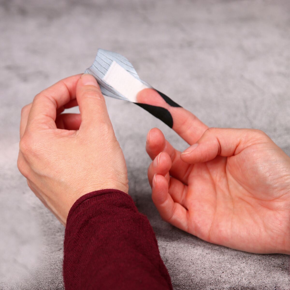 Hand legt schwarzes Fingerkuppenpflaster um einen Finger.