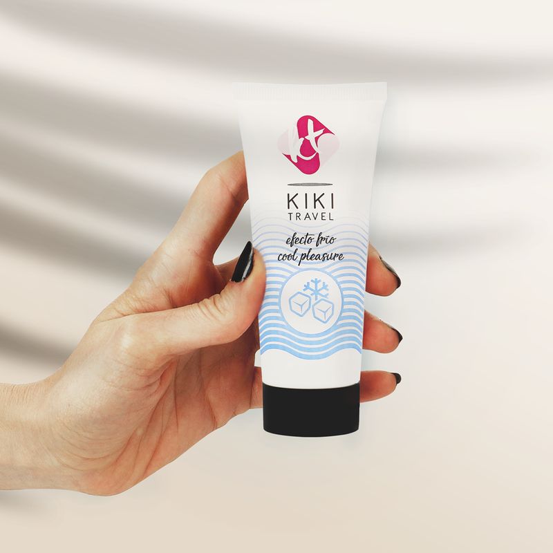 Hand hält weiße Tube mit KIKI TRAVEL Logo und Schriftzug „efecto frio cool pleasure“. Eiswürfel-Grafik.