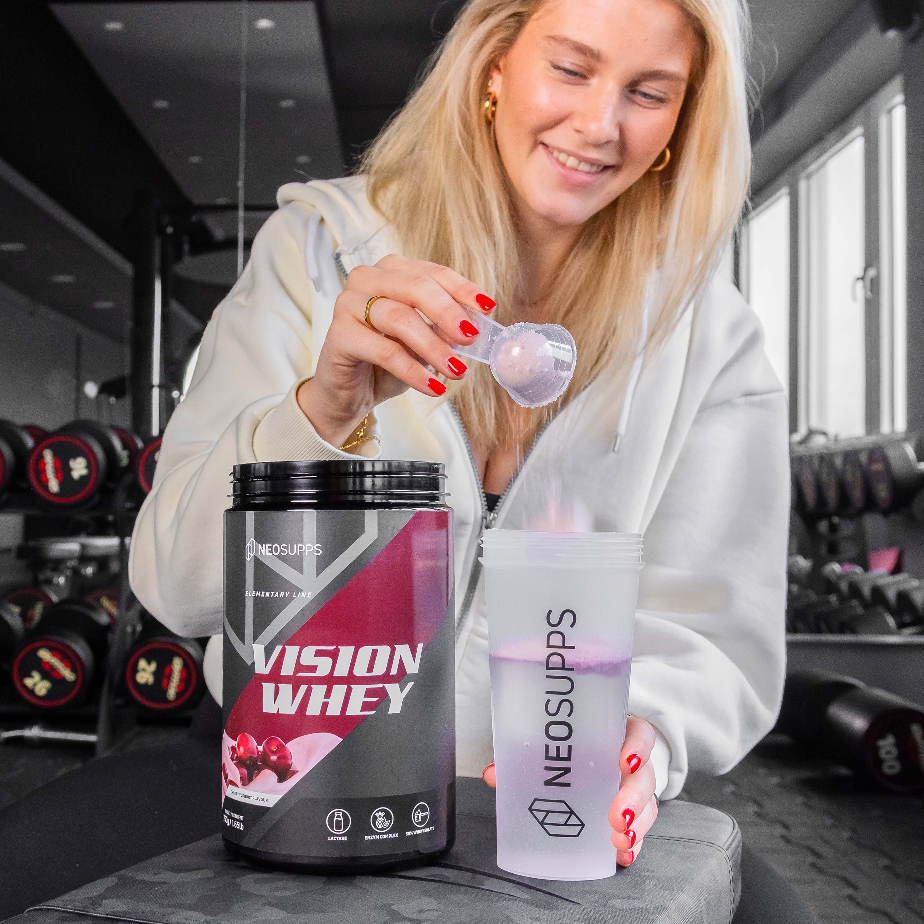 Frau mit Dose und Shaker. Dose Vision Whey, schwarze Dose mit rotem Etikett. Shaker mit Flüssigkeit und Messlöffel.