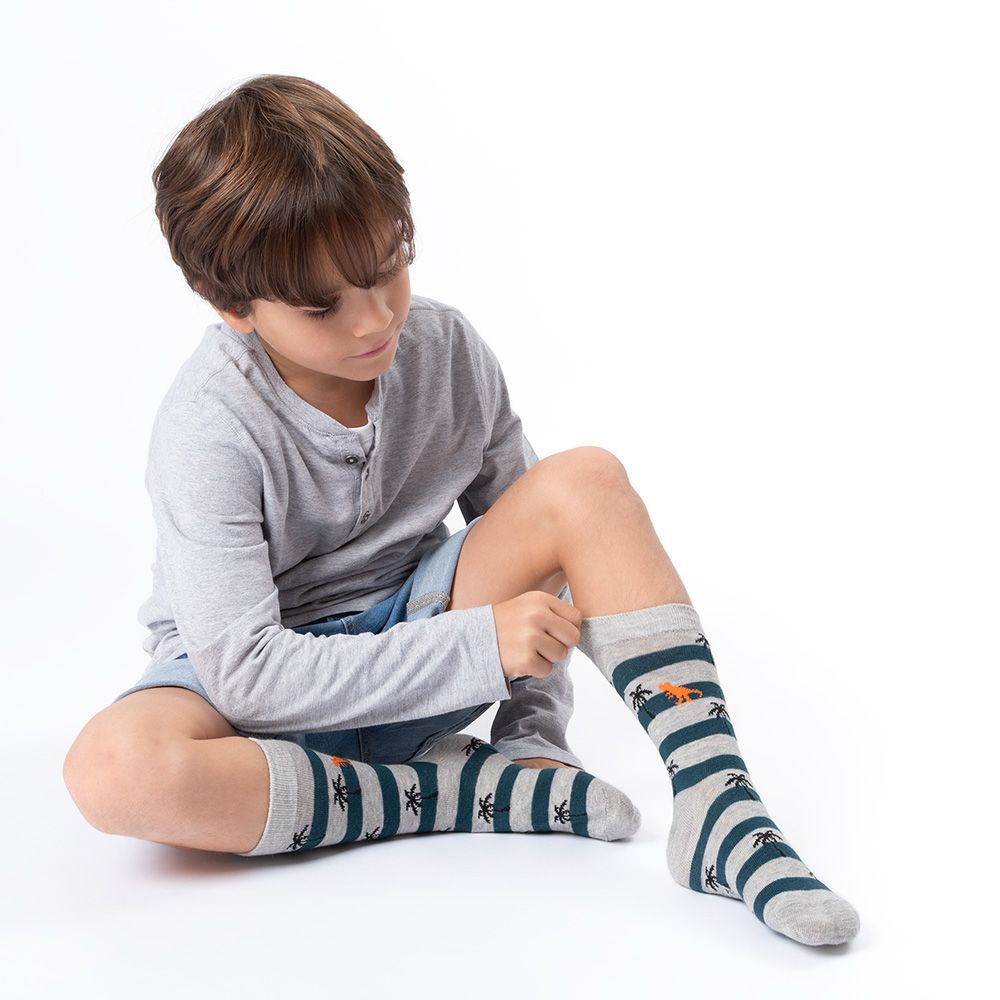 Kind sitzt und betrachtet Socken mit Streifen und Palmen. Graue Hose. Weißer Hintergrund.