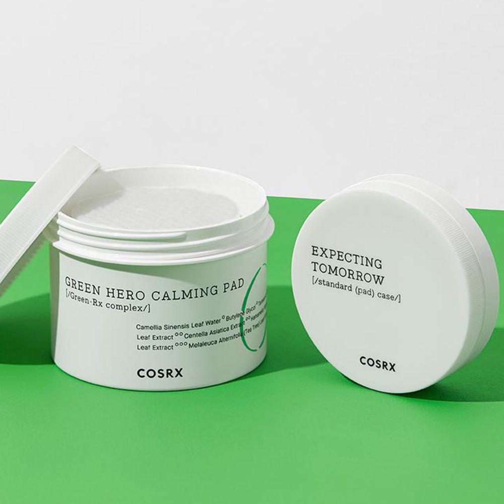 Weißer Behälter mit Pads und Deckel. Aufschrift: Green Hero Calming Pad, COSRX. Grüner Hintergrund.