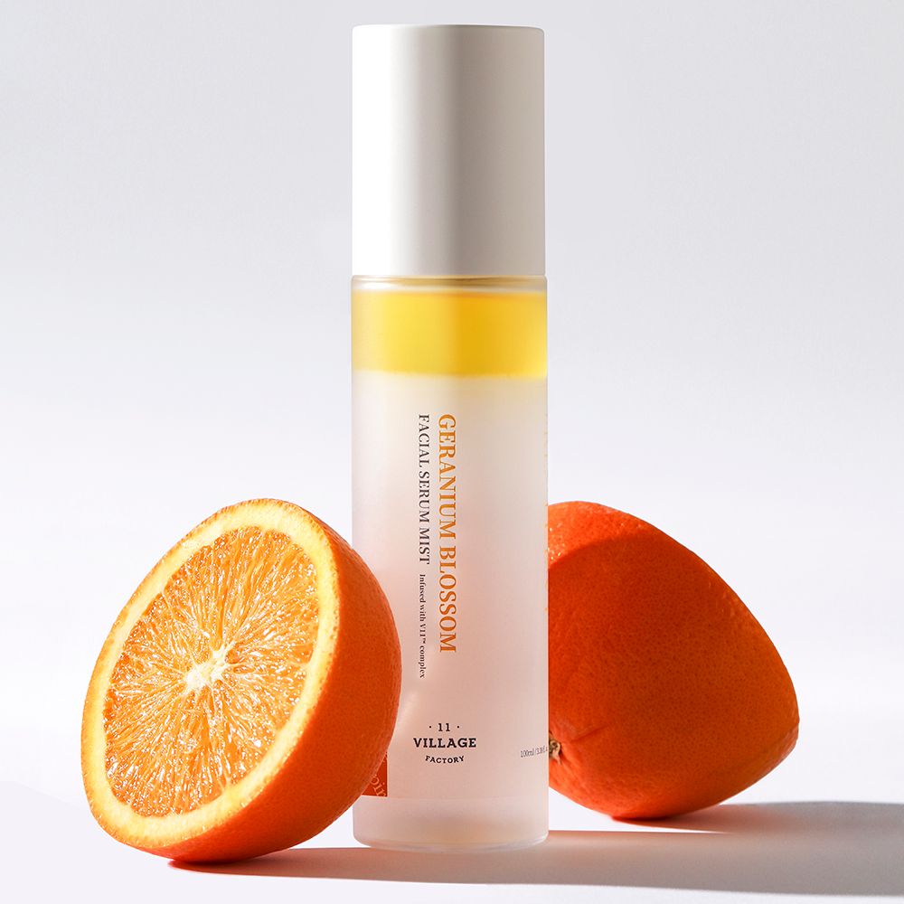 Produktflasche mit Orange und Orangenscheibe. Text: GERANIUM BLOSSOM, FACIAL SERUM MIST, -11- VILLAGE FACTORY. Weißer Deckel.