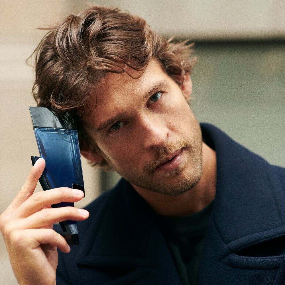 Mann hält eine blaue Flasche in Form eines Blitzes. Er trägt einen dunklen Mantel.