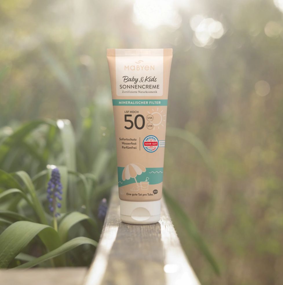 Sonnencreme-Tube auf Holz. Marke: MABYEN Baby & Kids. LSF 50. Mineralischer Filter. Wasserfest. Strandmotiv. Beige und weiß.