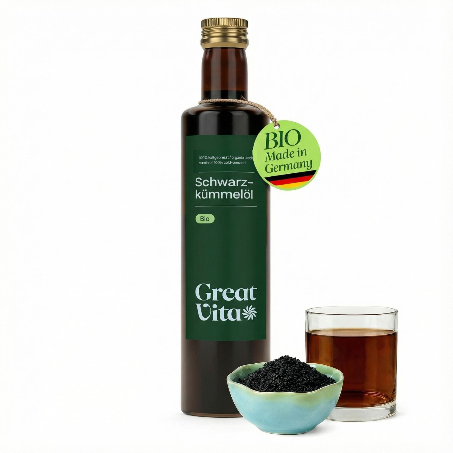 Flasche GreatVita Bio Schwarzkümmelöl, daneben ein Glas und eine Schale mit Samen. Anhänger mit Bio-Zertifizierung.