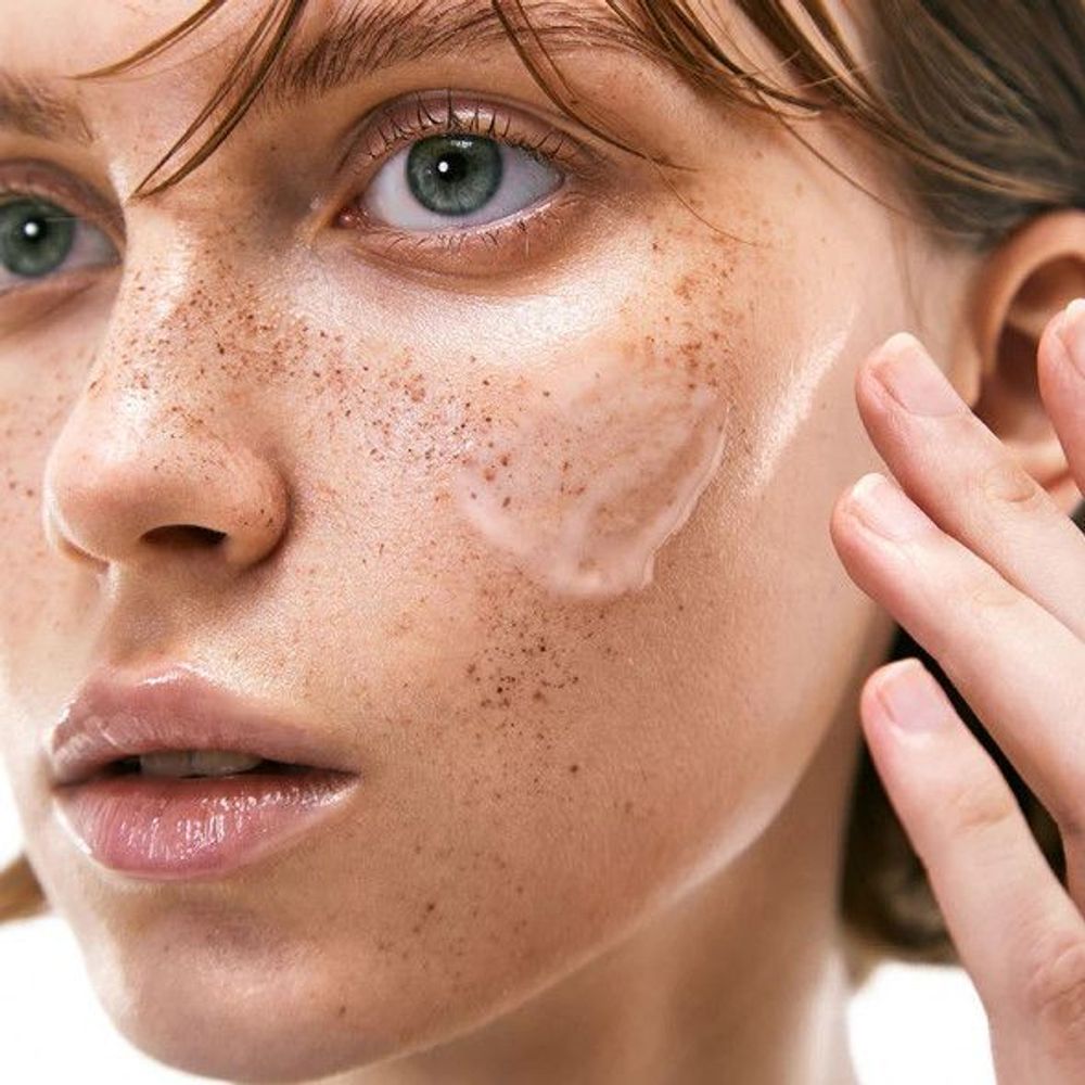 Nahaufnahme eines Gesichts. Auf der Haut wird ein Serum aufgetragen. Haut mit Sommersprossen.