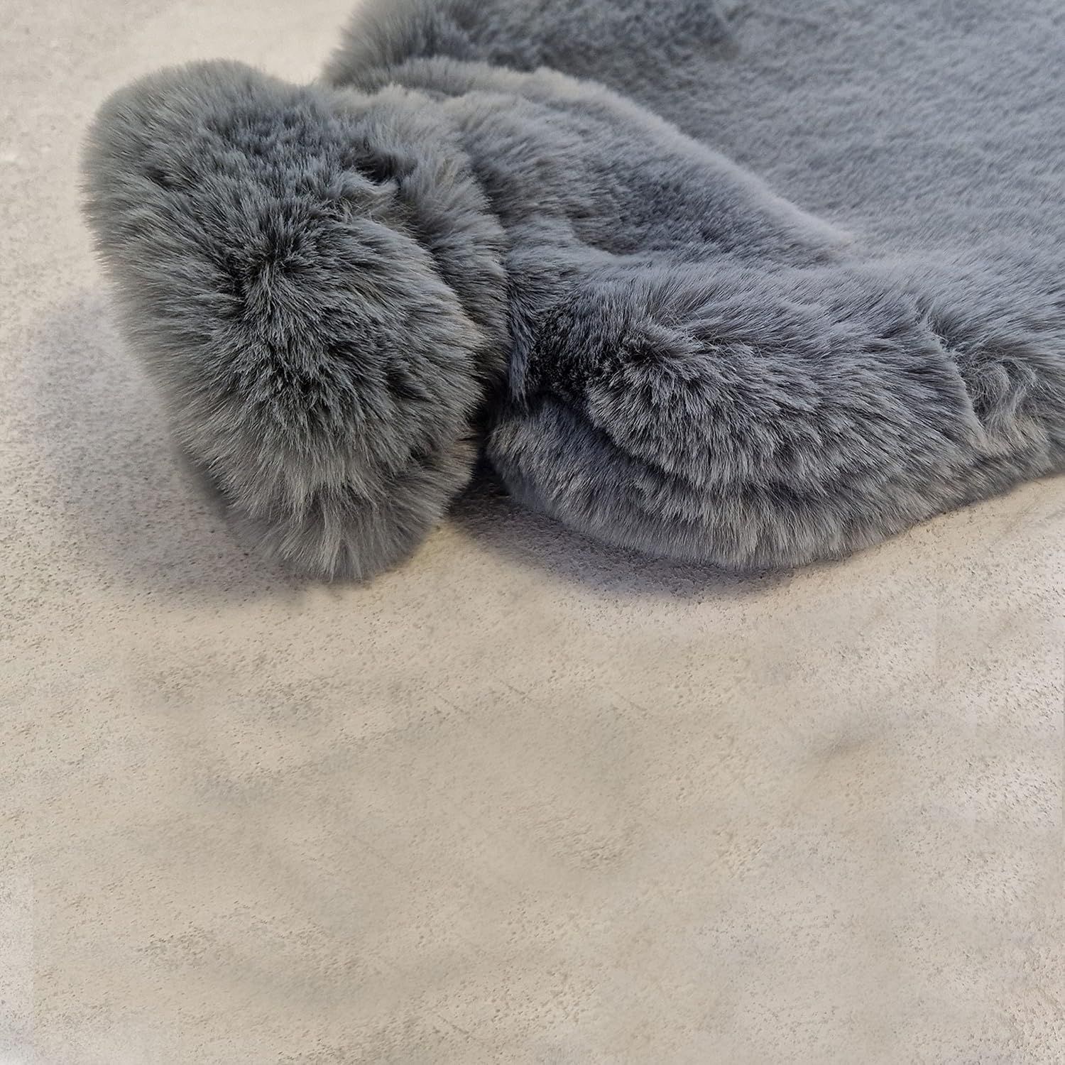 Graue Wärmflasche mit flauschigem Bezug. Rechteckige Form. Weiches Material. Nahaufnahme.