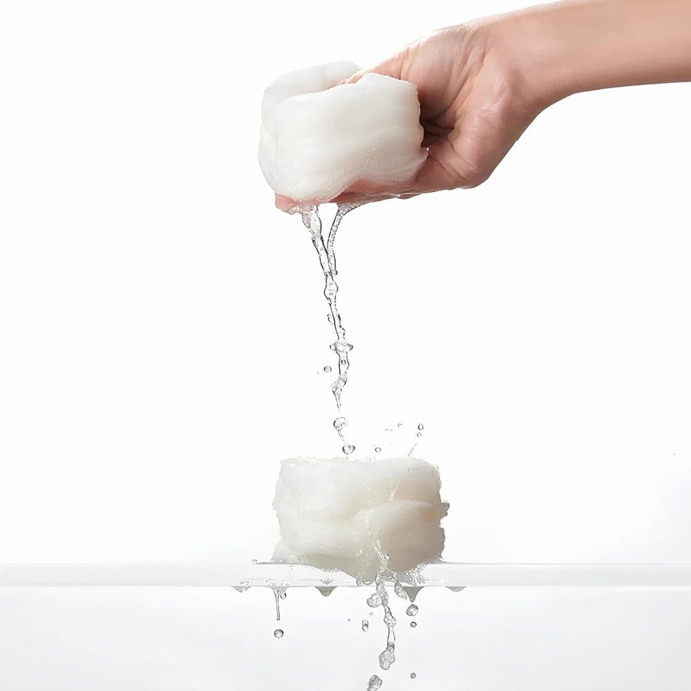 Zwei weiße, nasse Pads. Eines wird von einer Hand gehalten, Wasser tropft auf das andere.