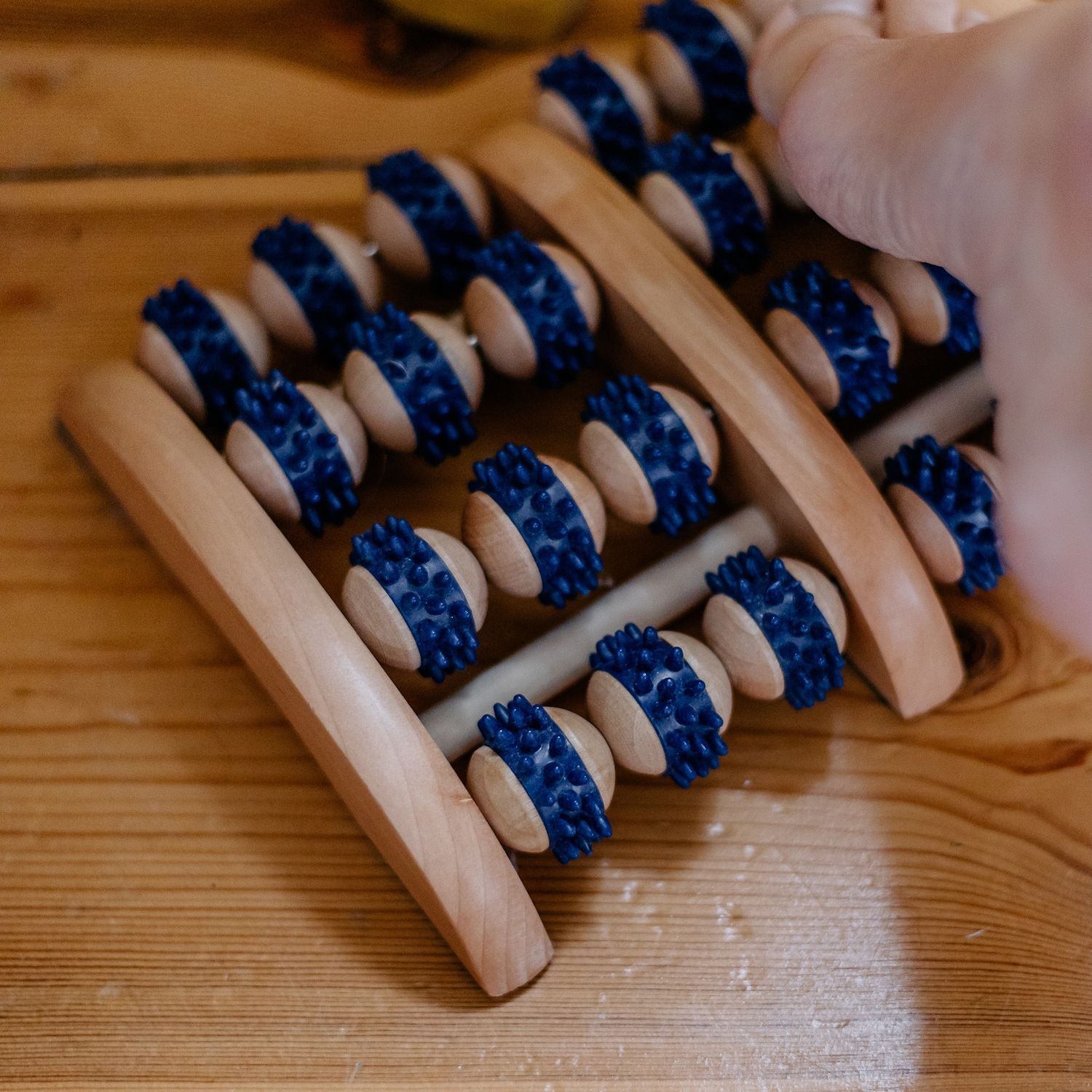 Ein hölzerner Massage-Roller mit blauen Noppen auf vier Holzrollen.