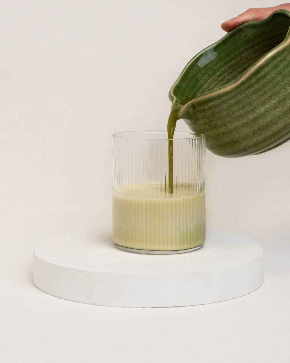 Grünes Getränk wird aus einer grünen Keramikschale in ein geriffeltes Glas gegossen.