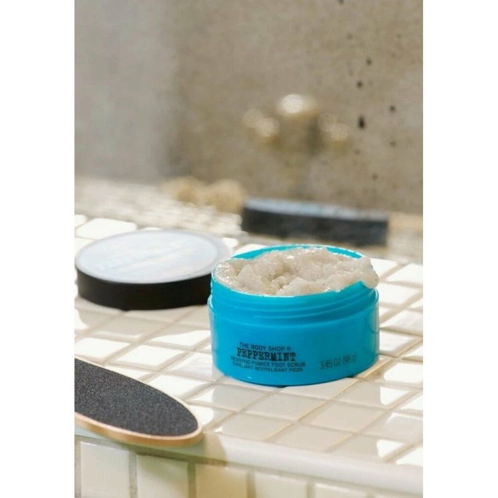 Blauer Tiegel mit Peeling. Daneben ein Fußfeile. Offener Deckel. Aufschrift: Peppermint, Reviving Pumice Foot Scrub. Marke: The Body Shop.