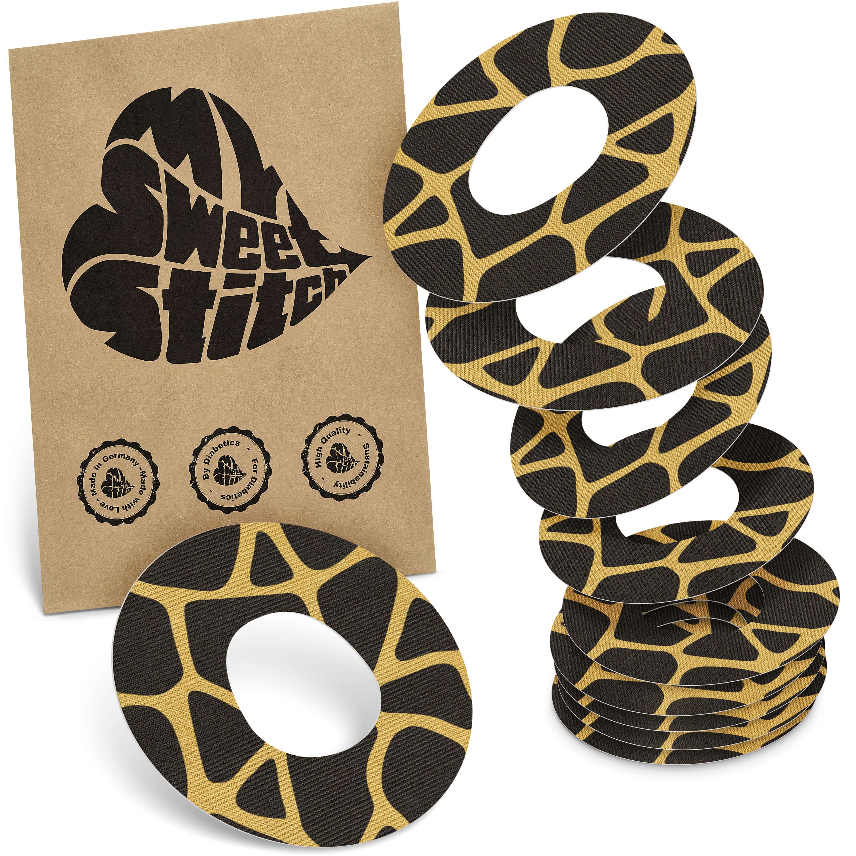 Fixierpflaster mit Giraffenmuster. Braune Verpackung mit Logo. Mehrere Pflaster liegen daneben.