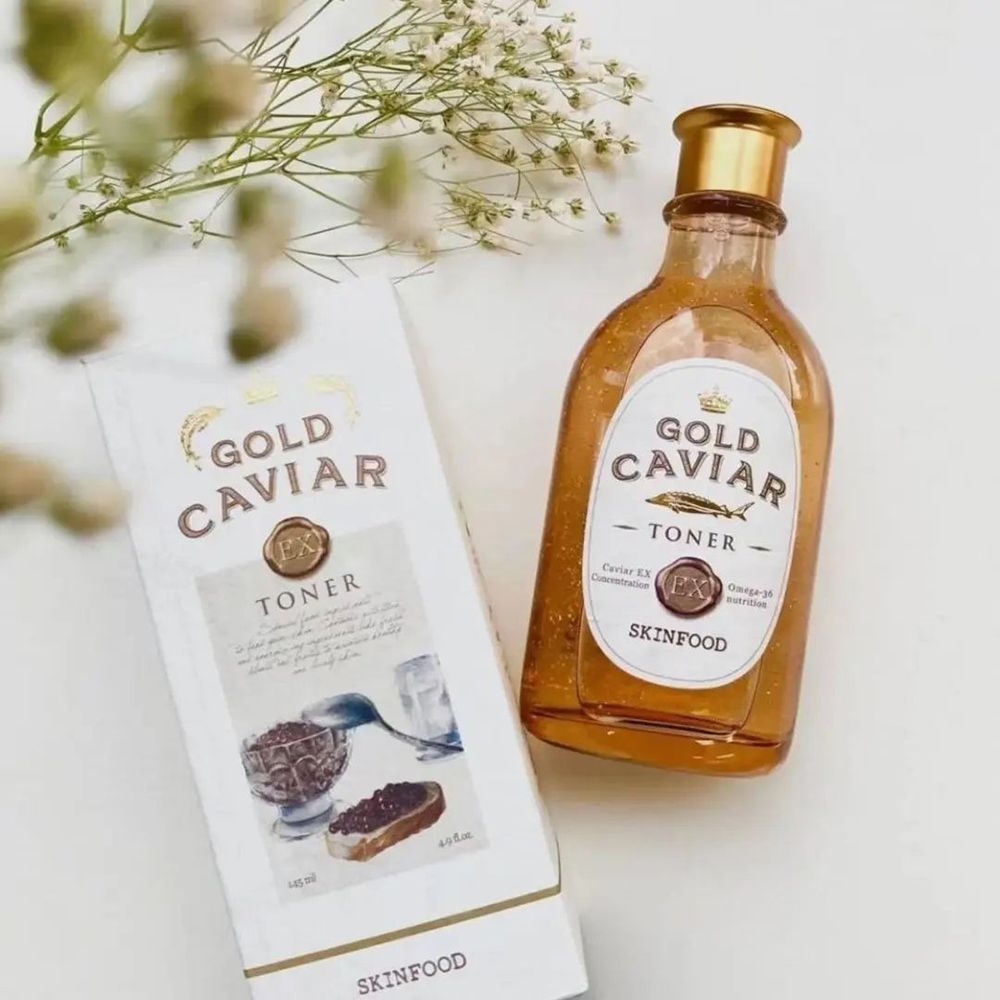 Gold Caviar Toner Flasche und Verpackung. Flasche mit goldfarbener Flüssigkeit. Verpackung mit Schriftzug Gold Caviar und SKINFOOD. Auf hellem Untergrund.
